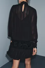 Vestido corto de viscosa color negro con cuello perkins y manga larga. Presenta un fajín de terciopelo integrado con bordados a tono y detalle de lazadas laterales.