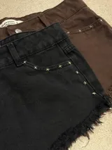 Short de jean negro con ruedo desflecado y detalle de tachas metálicas en forma de estrella en los bolsillos delanteros.