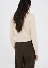 Cardigan de punto color beige, con escote en V y cierre frontal de botones con lazos decorativos.