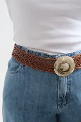 Cinto de cuero trenzado color marrón chocolate, con hebilla circular metálica grabada y detalle central de piedra natural.