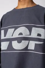 Buzo oversize de corte boxy, confeccionado en algodón rústico de alto gramaje en color beige. Presenta cuello redondo con borde crudo, mangas largas y una estampa frontal con el texto VCP delimitado por líneas horizontales blancas.