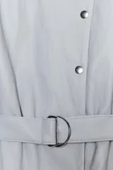 Vestido corto de efecto piel en color celeste grisáceo, con cuello redondo, manga larga con puños elásticos y hombreras. Presenta un cierre frontal con botones a presión y un cinturón ajustable del mismo tejido con hebilla metálica.