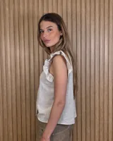 Musculosa a rayas verdes y blancas, con cuello alto fruncido, cierre frontal con botones y volados en los hombros.