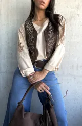 Chaleco de gamuza color chocolate con bordados decorativos en hilo claro y detalles de tachas metálicas en el frente. Presenta cierre frontal con botones forrados.