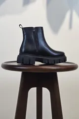 Bota de caña corta color marrón, con cierre lateral y suela track negra de goma con plataforma.