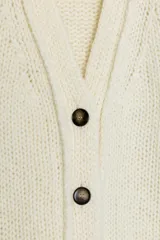 Chaqueta de punto de lana con cuello en pico, manga larga y cierre frontal con botones oscuros. Presenta un diseño de tejido grueso y holgado.