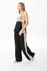 Pantalón sastrero de lino color negro con una guarda lateral de broderie color crudo que recorre el lateral desde la cintura hasta el bajo. El pantalón es de corte ancho y fluido.