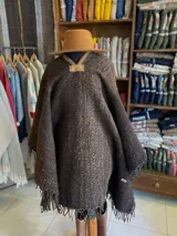Poncho de lana virgen tejido en telar con diseño geométrico a rayas en tonos gris, marrón y celeste, con apliques de cuero en el escote y flecos en el ruedo.