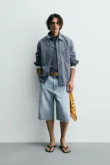 Camisa de manga larga con cuello solapa, bolsillo de plastrón en el pecho y cierre frontal con botones a presión. Presenta un patrón de cuadros vichy en tonos de azul desgastado.