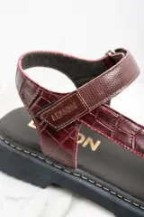 Sandalias de cuero color marrón con textura tipo cocodrilo, plataforma plana y tira ajustable con hebilla.