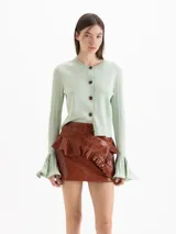 Minifalda de cuero ovino color marrón, de tiro medio-alto y silueta entallada. Presenta un recorte diagonal con un volado aplicado de forma asimétrica.