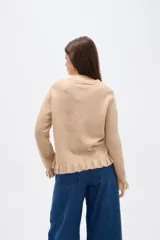 Saco de punto color gris, con cuello redondo, cierre frontal con botones y detalle de volados en la tapeta y el ruedo. Presenta mangas largas con puños acampanados.