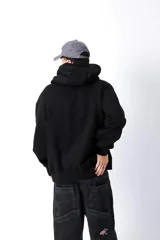 Hoodie negro de frisa con capucha y bolsillo canguro. Presenta un aplique rectangular en el pecho con texto en verde lima.