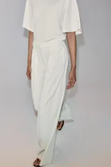 Pantalón wide leg de tiro medio, color blanco con diseño de rayas diplomáticas a contraste, bolsillos laterales y de vivo en la espalda, pinzas en el delantero y cierre frontal con cremallera, botón y ganchos metálicos.