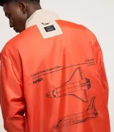 Campera rompevientos color beige con capucha, cierre frontal y bolsillos laterales. Presenta estampado de la NASA en el pecho, parche circular en la manga derecha y bandera de Estados Unidos en la manga izquierda.