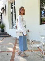 Cartera tipo sobre color crudo, confeccionada en cuero, con correa larga de cuero marrón y costuras decorativas en contraste.