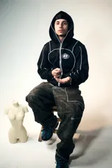 Campera hoodie negra con cierre frontal, bolsillos tipo canguro, capucha con cordón ajustable y detalles de ribete blanco. Presenta un logo con un globo terráqueo y el número 27 en el pecho y un estampado de una estrella con incrustaciones en la espalda.