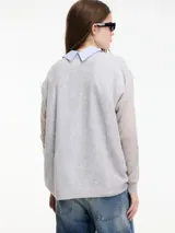 Sweater de punto fino color gris claro, con cuello en V y mangas largas. El tejido parece ser ligeramente transparente o muy liviano.