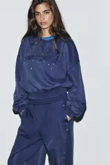 Sudadera de cuello redondo y manga larga con efecto lavado. Presenta texto bordado en el frente y aplicación de tachas decorativas. Posee puños y ruedo con acabado en rib.
