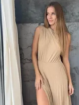 Vestido largo de un solo hombro, confeccionado en tela plisada con acabado brillante. Presenta un diseño entallado en la cintura con una falda fluida que incluye una abertura lateral pronunciada.