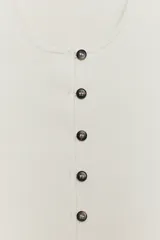 Chaqueta corta de punto color blanco crudo, con escote redondo pronunciado y cierre frontal con botones oscuros. Presenta mangas cortas abullonadas con frunces.