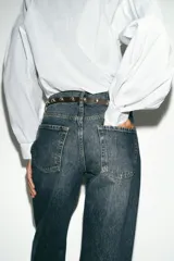 Jeans de tiro alto con diseño de cinco bolsillos y corte recto que se estrecha hacia el tobillo. Incluye un cinturón negro con tachas metálicas. Cierre frontal con cremallera y botón.