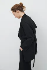 Trench simil gamuza color marrón, con cuello de solapa muesca, cuatro botones delanteros, bolsillos laterales y cinturón a la altura de la cintura.