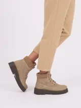 Borcego de caña corta color beige, con cordones al tono, cuello acolchado y suela de goma dentada en color marrón oscuro.