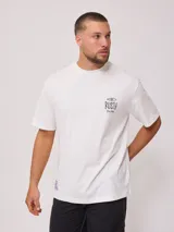 Remera blanca de algodón con cuello redondo y manga corta. Presenta un pequeño estampado frontal con el logo de Rusty y un diseño de tabla de surf.