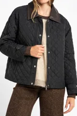 Campera negra de diseño capitoneado con cuello de solapa en contraste color marrón. Presenta cierre frontal con cremallera y botones a presión, mangas largas con puños ajustables y un corte recto.