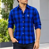 Camisa de manga larga con diseño de cuadros en tonos de azul y negro, confeccionada en algodón. Cuenta con cuello camisero, cierre frontal de botones blancos y un sutil bordado blanco en el pecho.