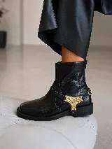 Bota corta de cuero negro con punta cuadrada, taco bajo y detalle de aplique metálico dorado en el lateral. Cuenta con cierre posterior y diseño de estilo sport.