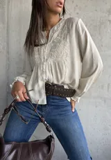 Camisa beige de manga larga con cuello mao y escote en V. Presenta detalles bordados en el canesú y los hombros, y volados en los puños.