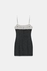 Vestido corto entallado con estampado de lunares, tirantes finos ajustables y escote redondo con detalle de frunces y lazada frontal. Presenta un diseño combinado con contraste de colores en la parte superior y cierre de cremallera oculta en la espalda.