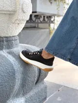 Zapatillas deportivas negras de cuero, con cordones y suela de goma blanca con base marrón.