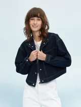 Campera de denim azul oscuro, estilo trucker, con cuello camisero y cierre frontal de botones metálicos. Presenta costuras contrastantes en color claro.