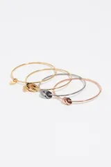 Set de cuatro pulseras rígidas tipo esclava con acabados metálicos en tonos dorado, plateado y oro rosa. Presentan dijes circulares con detalles en esmalte negro y un dije en forma de corazón.