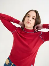 Polera de cuello alto confeccionada en tela rib color rojo, con costuras a la vista en contraste color celeste. Presenta hombreras y mangas largas.