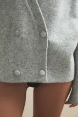 Cardigan de punto gris claro, con escote en V profundo, cierre frontal cruzado con botones y mangas largas holgadas.