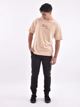 Remera color beige con estampado frontal de texto en color marrón. Corte oversize.
