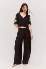 Blusa corta de color negro con escote en V, mangas cortas y bordados florales en contraste sobre las mangas.