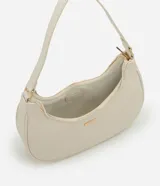 Cartera tipo baguette de diseño minimalista en color beige, confeccionada en poliuretano con acabado liso. Presenta cierre superior con cremallera, asa ajustable y detalles metálicos en tono dorado claro, incluyendo una placa con el logo de la marca en el frente.
