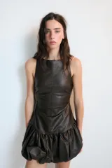 Vestido corto de efecto piel con cuello barco y diseño sin mangas. Presenta un bajo abullonado con elástico interior y cierre de cremallera en la espalda.
