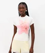 Remera baby tee de algodón color blanco, con cuello redondo, manga corta y un gran estampado frontal de una flor de lirio en tonos rosados con aplicaciones de pedrería.