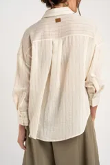 Camisa de manga larga con patrón de rayas sutiles, corte holgado, cuello camisero, cierre frontal con botones y un bolsillo aplicado en el pecho.