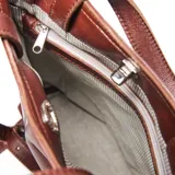 Bandolera grande de cuero color marrón, con diseño cuadrado, doble asa de mano y correa larga ajustable y extraíble. Cuenta con cierre superior y logo de la marca grabado en el frente.