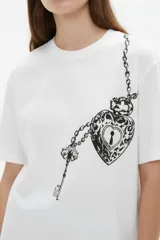 Remera blanca de manga corta y cuello redondo, de corte holgado, con un gran estampado frontal en color negro que simula un collar de cadenas con un candado en forma de corazón y una llave.