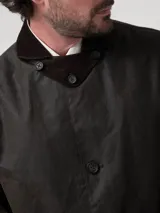 Chaqueta de estilo clásico confeccionada en tela encerada impermeable, con cuello de cotelé, cierre frontal con botones y bolsillos delanteros con solapa.