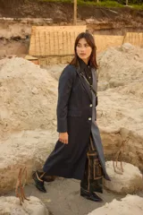 Tapado largo de sastrería con diseño bicolor y asimétrico. Una mitad presenta un tejido negro con rayas diplomáticas, mientras que la otra mitad es de un tejido a cuadros en tonos tierra. Cuenta con botones de nácar, bolsillos con tapa y abertura trasera.