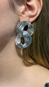 Caravanas de diseño moderno compuestas por dos eslabones entrelazados con acabado metálico plateado y superficie texturizada.